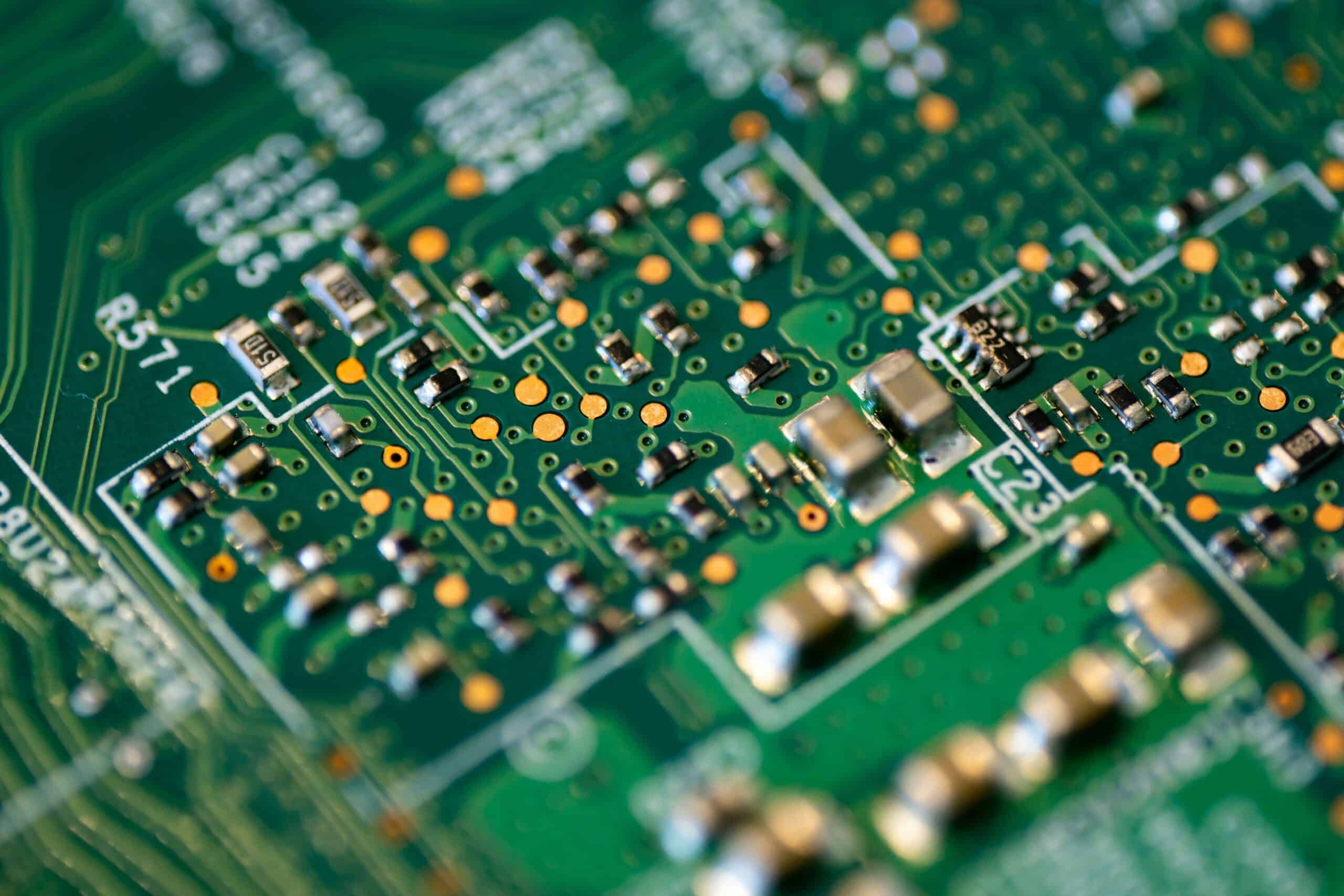 Close-up image of a green printed circuit board (PCB) with various electronic components such as DC-DC Wandler, resistors, capacitors, and integrated circuits.